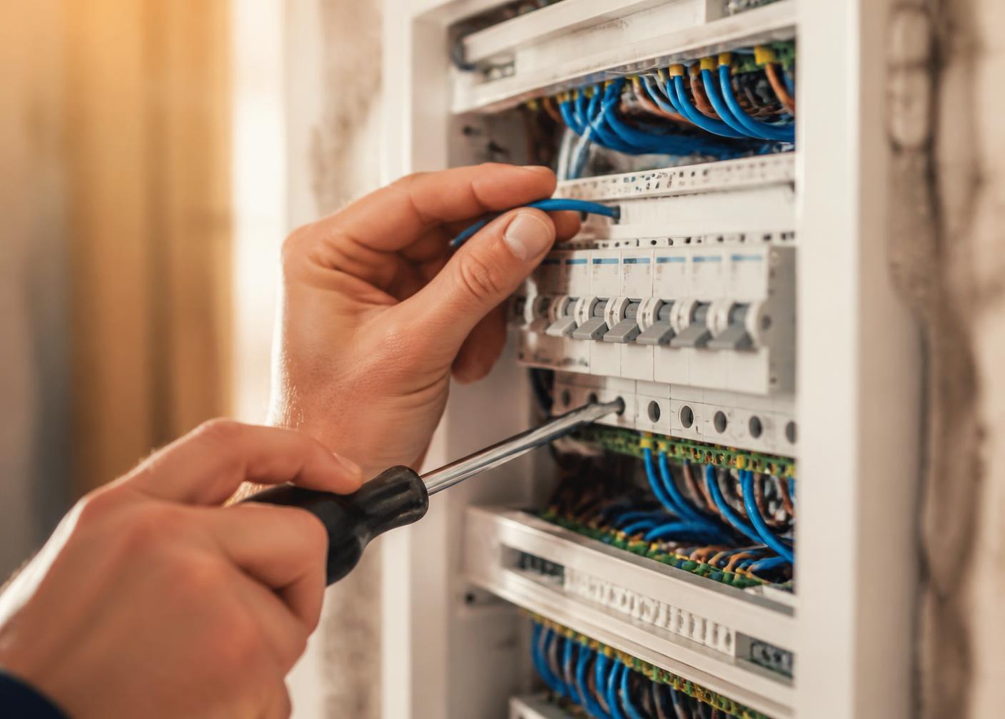 Närbild på elektrikerns händer som kopplar in kablar i en elcentral